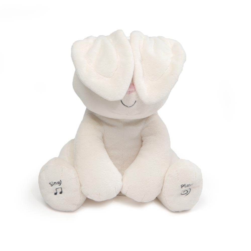 Flora animated baby plush bunny toy in white, sitting and playing peek-a-boo with its ears covering its eyes. Features interactive 'Sing' and 'Play' embroidered feet.
