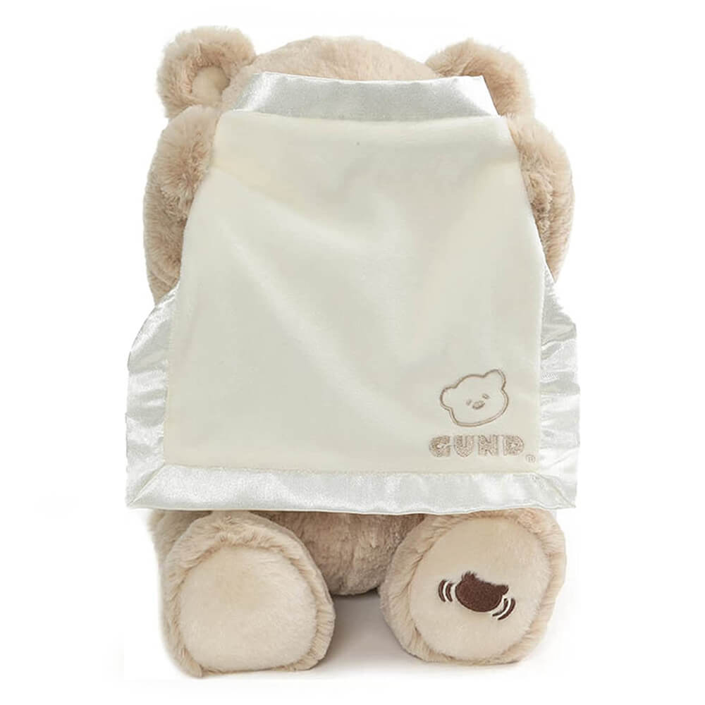 GUND Peek-a-Boo Bear plush toy hiding behind a satin-trimmed blanket during peekaboo play.