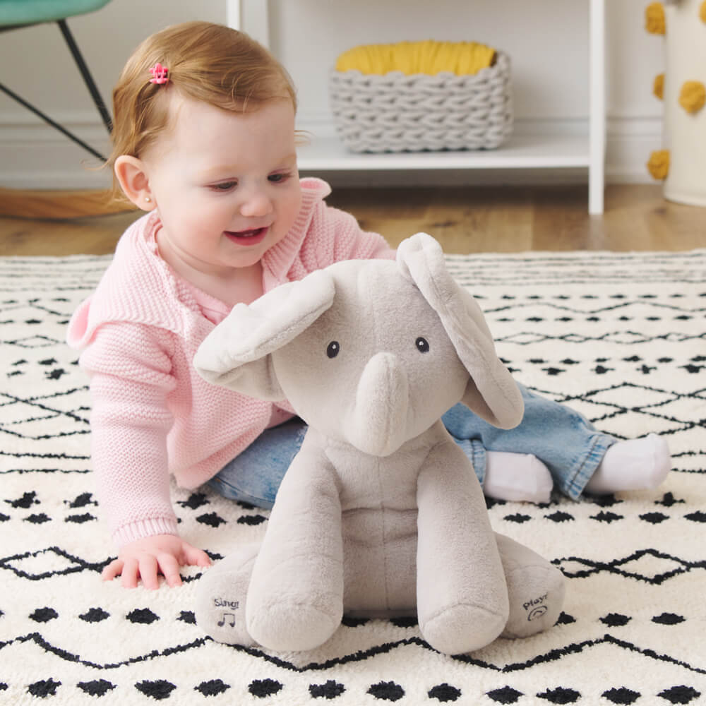 Baby girl playing with a soft grey elephant plush toy with large floppy ears