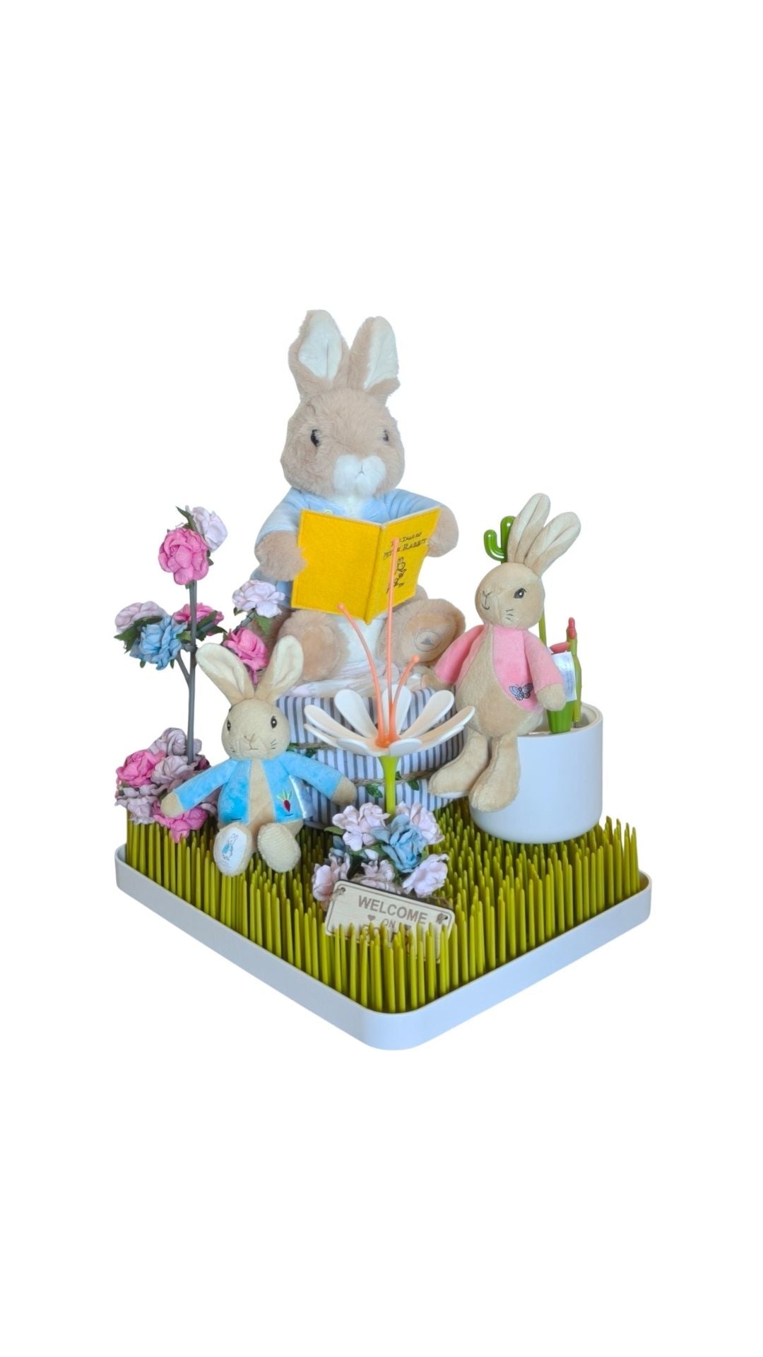 Peter Rabbit gift display on a green grass rack, featuring a large reading rabbit, two small plushies, flowers, and a sign.