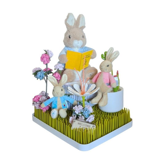 Peter Rabbit gift display on a green grass rack, featuring a large reading rabbit, two small plushies, flowers, and a sign.