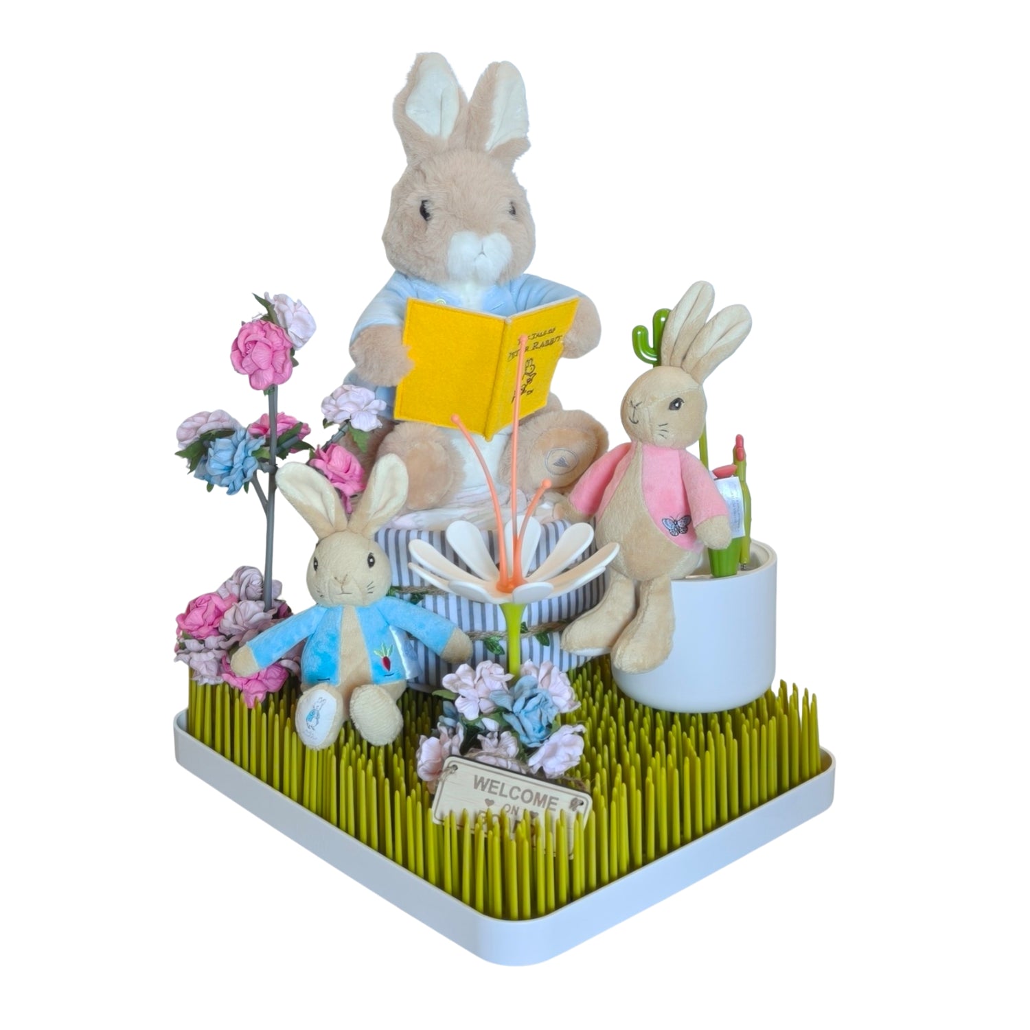 Peter Rabbit gift display on a green grass rack, featuring a large reading rabbit, two small plushies, flowers, and a sign.