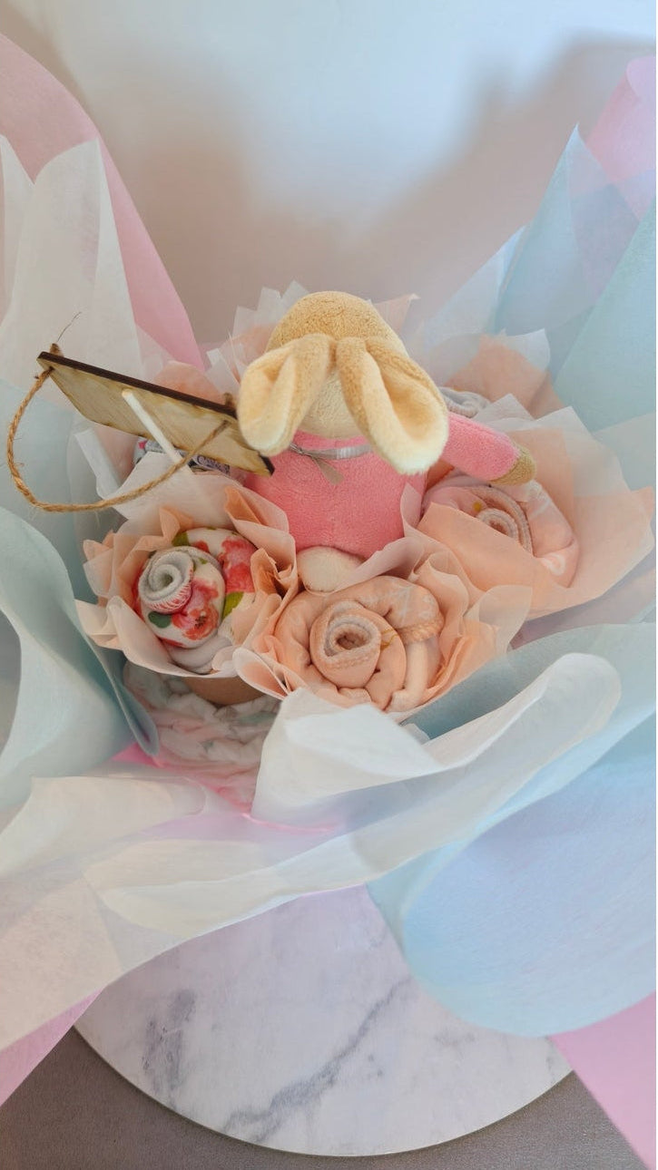 Back view of a baby girl bouquet showing a plush rabbit in a pink jacket and rolled pink bibs