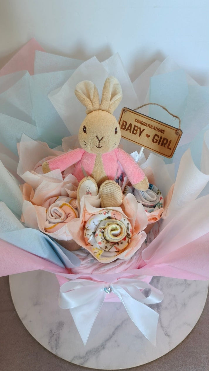 Back view of a baby girl bouquet showing a plush rabbit in a pink jacket and rolled pink bibs