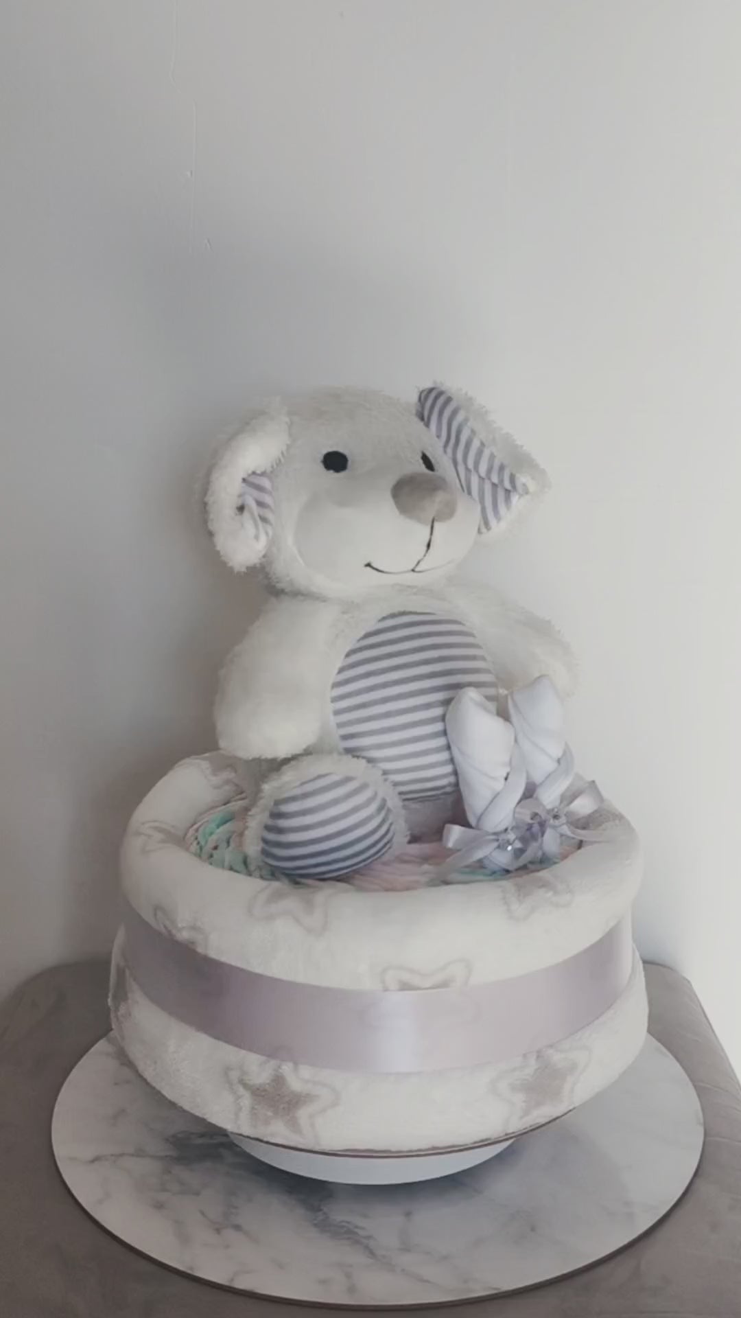 360-degree view of a unisex puppy dog baby shower nappy cake, featuring a soft plush toy, baby mittens, and a star-patterned blanket base tied with a silver ribbon.