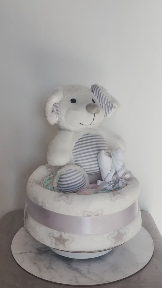 360-degree view of a unisex puppy dog baby shower nappy cake, featuring a soft plush toy, baby mittens, and a star-patterned blanket base tied with a silver ribbon.