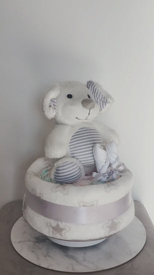 360-degree view of a unisex puppy dog baby shower nappy cake, featuring a soft plush toy, baby mittens, and a star-patterned blanket base tied with a silver ribbon.