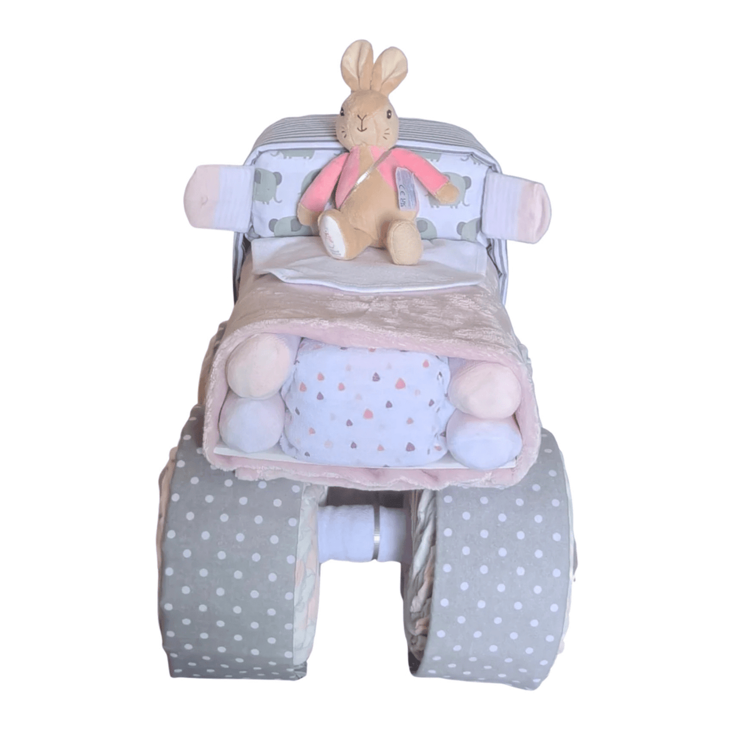 Front view of a Bunny baby girl truck nappy cake gift set featuring rolled infant garments, pink receiving blankets, and grey polka-dot wheels.