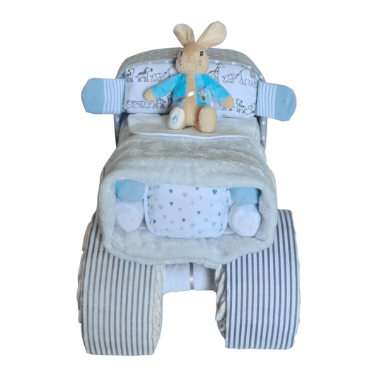 Front view of a Peter Rabbit baby boy truck nappy cake gift set featuring rolled infant garments, light blue receiving blankets, and striped wheels.